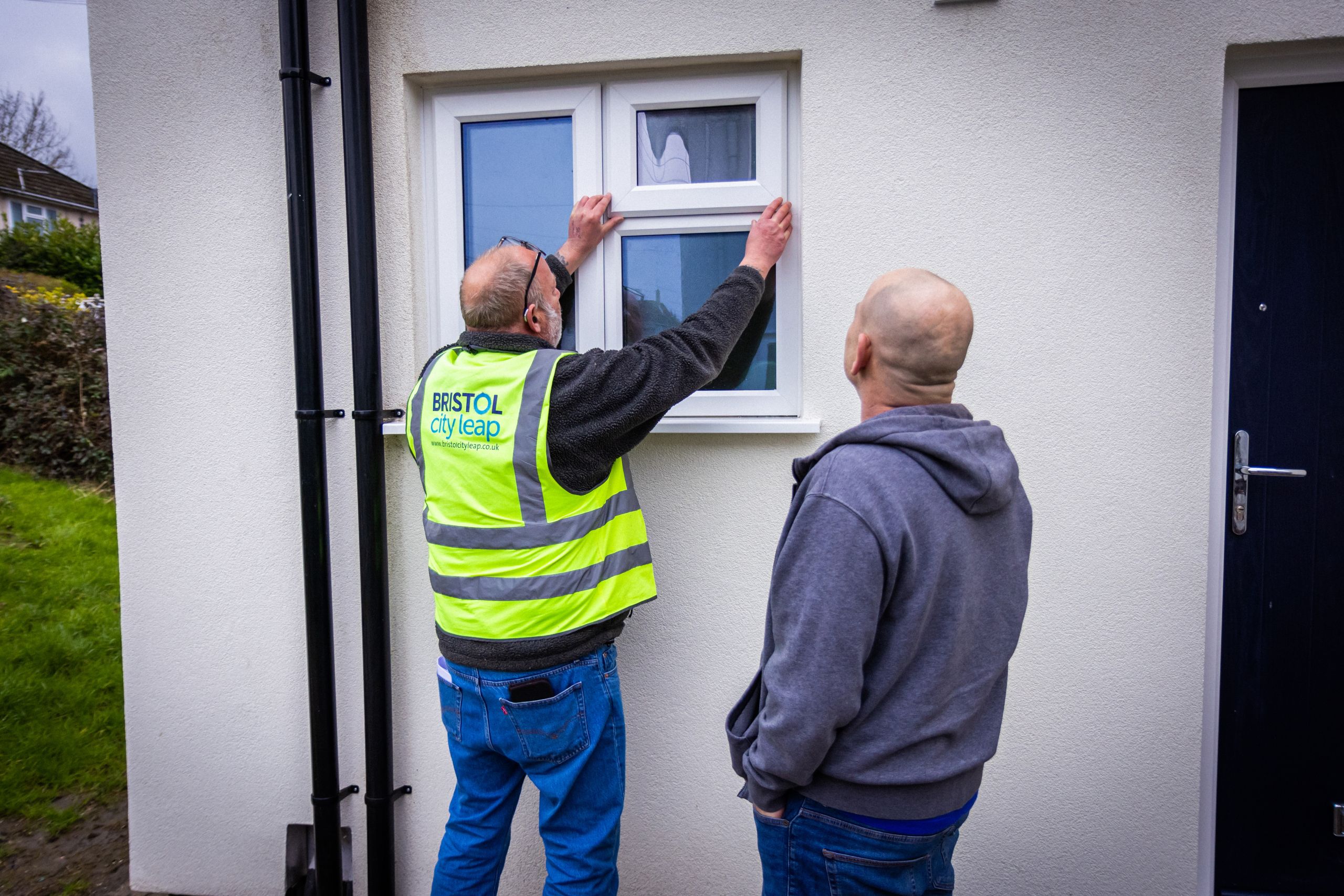 A team member wearing a Bristol City Leap high-vis jacket inspects a newly installed window alongside a resident during for a retrofit project.