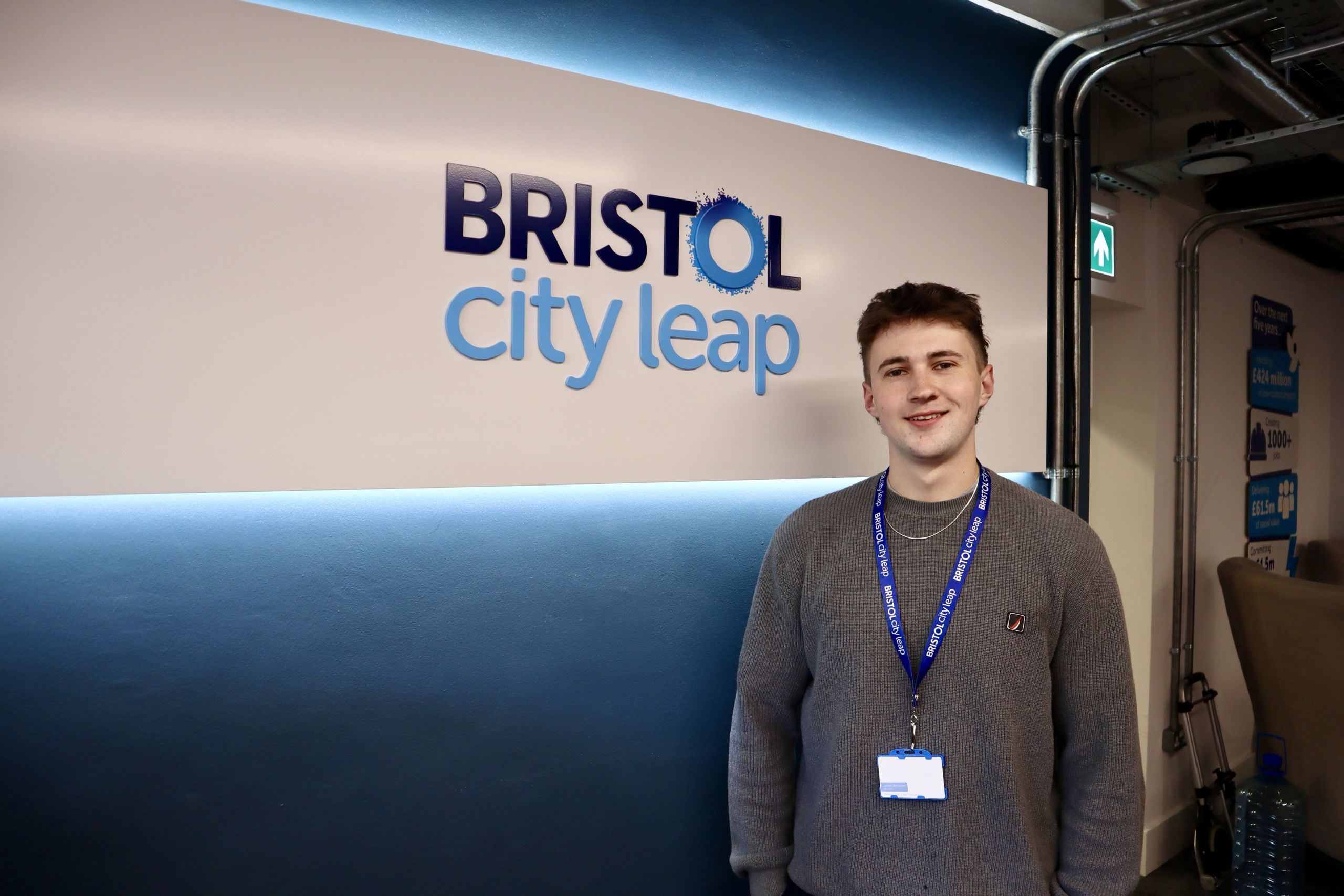 A Bristol City Leap intern smiles while standing next to the Bristol City Leap sign inside their office.