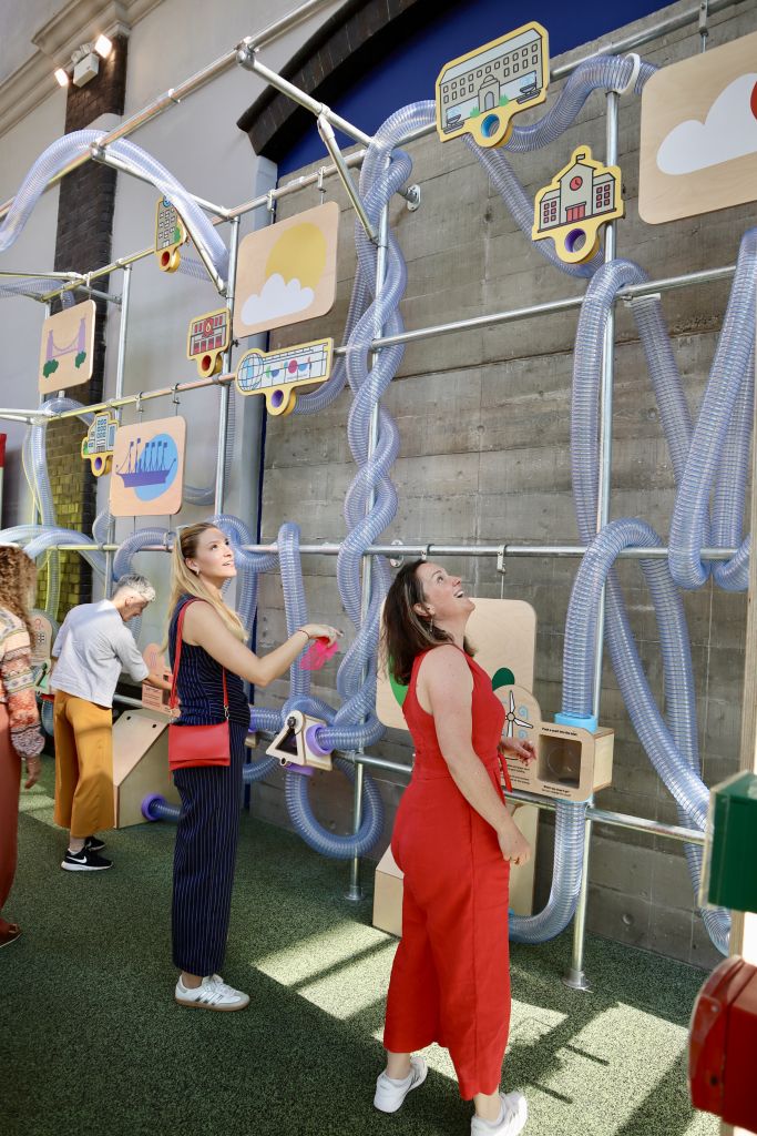 Visitors engaging with interactive sustainability displays featuring transparent tubes, illustrated landmarks and educational panels about Bristol’s environment and energy systems.